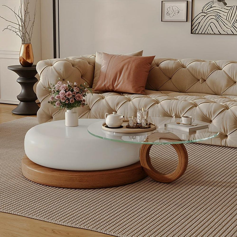 White and clear-glass coffee table with overlapping round surfaces and a wood-look ring base beside a tufted cream sofa