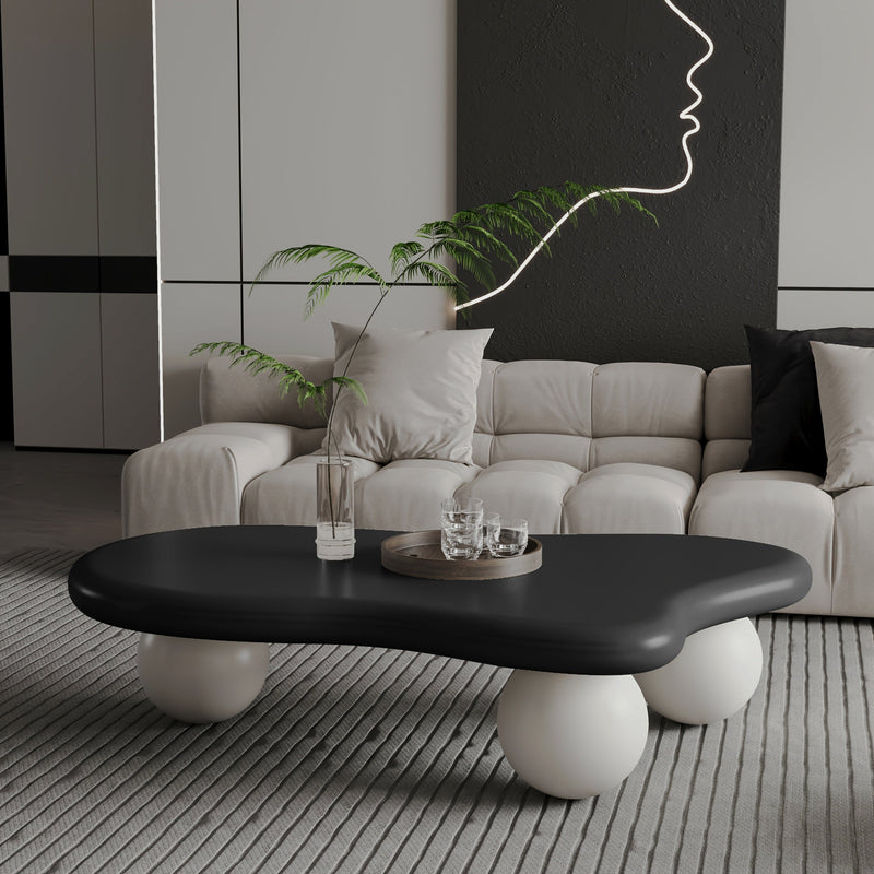 Black cloud-shaped coffee table with three white ball legs in front of a cream sofa