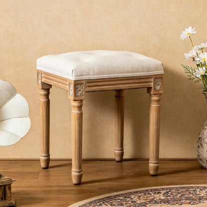 Beige tufted vanity stool with carved natural-tone wood legs in a bedroom
