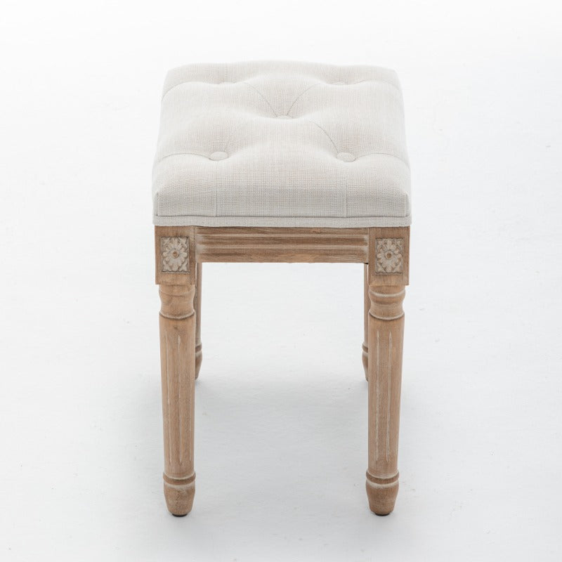 Narrow side view of the beige stool's tufted seat and carved wood corner