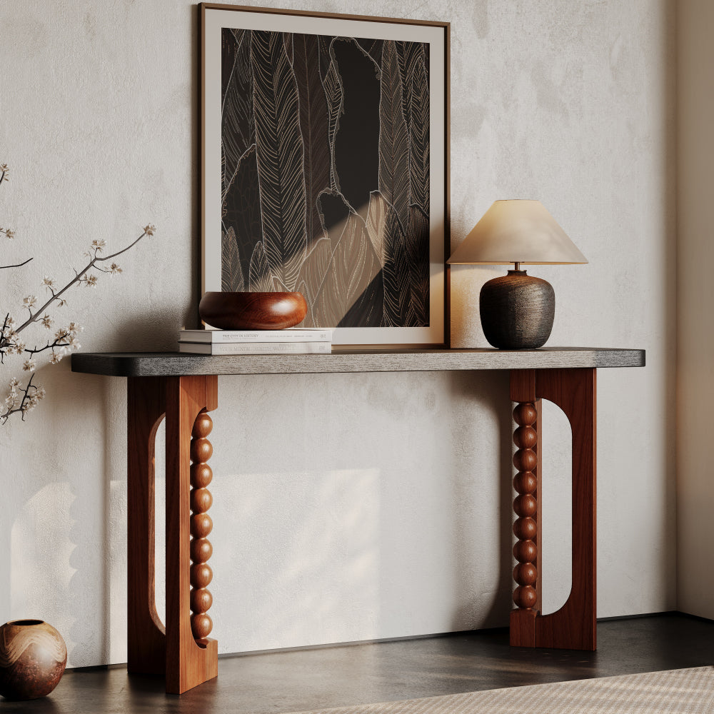 Console with a dark top and warm brown beaded supports styled below framed artwork.