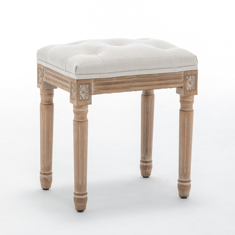 Three-quarter view of the beige stool's button-tufted seat and carved wood frame