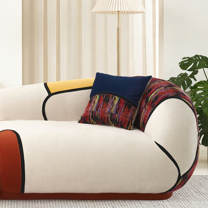 Close-up of the sofa’s rounded arm, cream upholstery, dark piping and patterned accent pillow.