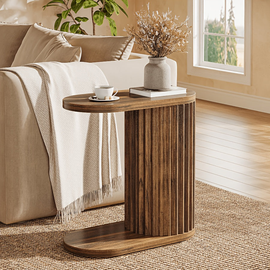Fluted C-shaped table beside a sofa with a cup and books on top.