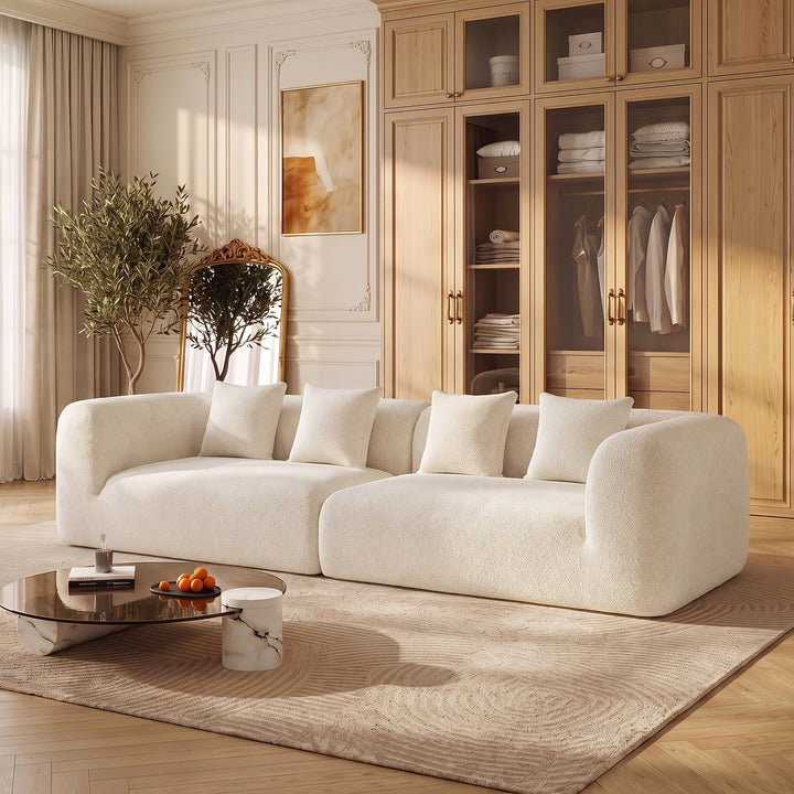 Curved modular sofa in light neutral upholstery with four pillows in a furnished living room.
