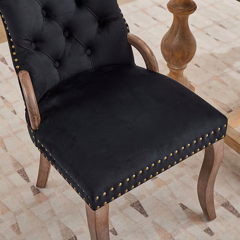 Black velvet dining chair with a tufted back, wood handle, and curved wood legs