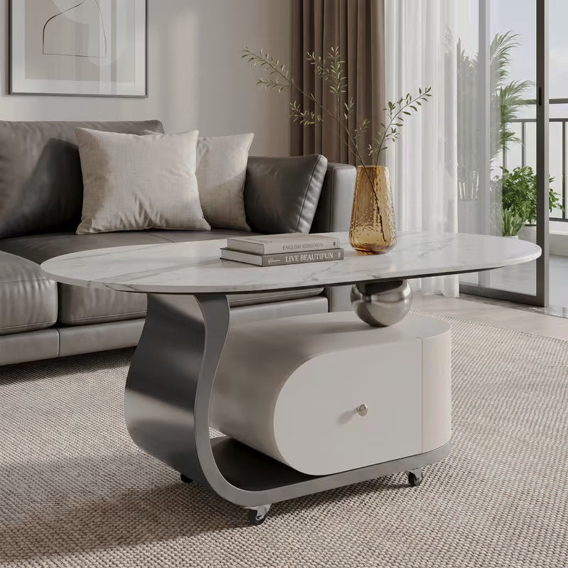 Oval cream and silver-tone coffee table with a stone-patterned top, drawer and caster wheels beside a gray sofa
