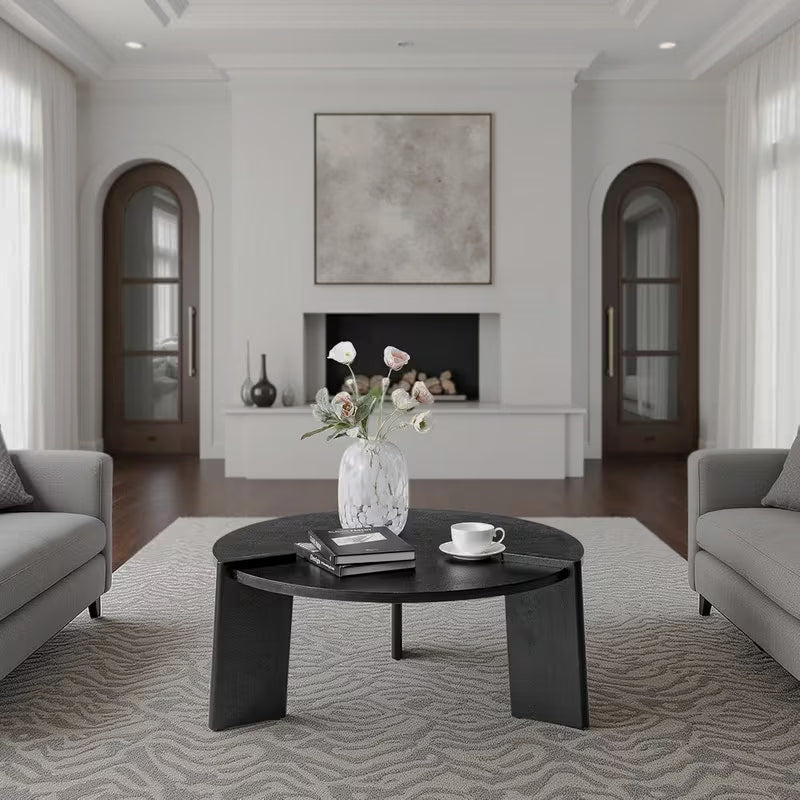 Black round coffee table with three broad slab legs and raised edge details in a living room