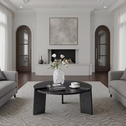 Black round coffee table with three broad slab legs and raised edge details in a living room