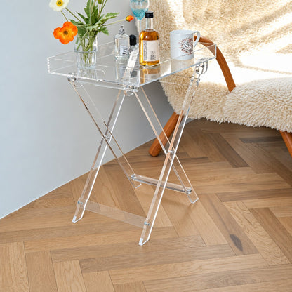 Luma Folding Tray Table — clear acrylic tray and crossed folding frame beside a sheepskin chair, full lifestyle view