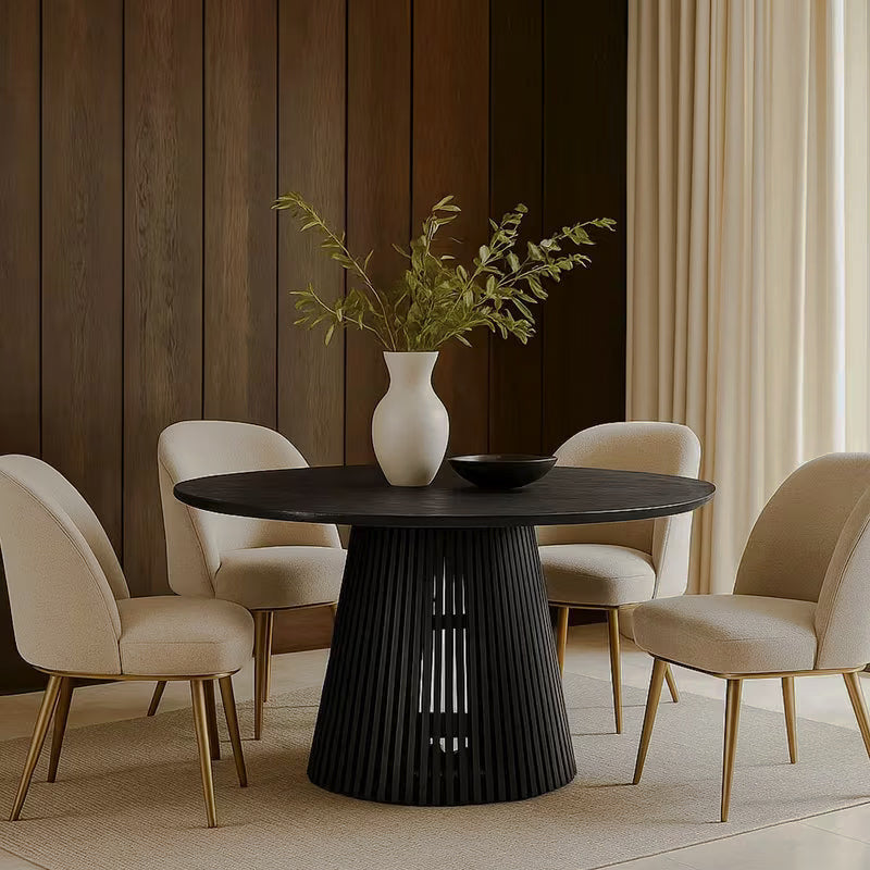 Round black dining table with cream chairs beside a dark paneled wall