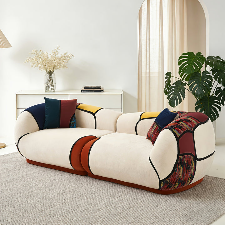 Three-quarter view of the cream colorblock sofa with rounded cushions and two decorative pillows.