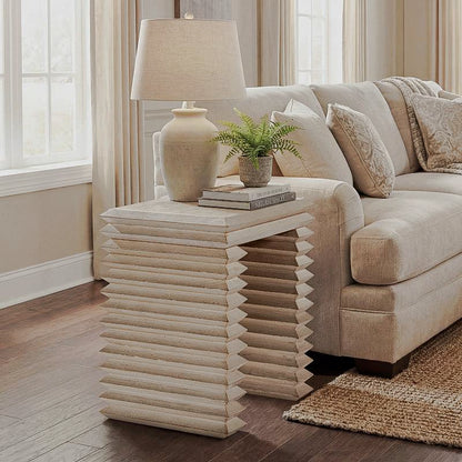 Whitewashed geometric side table with stacked horizontal ridges beside a cream sofa