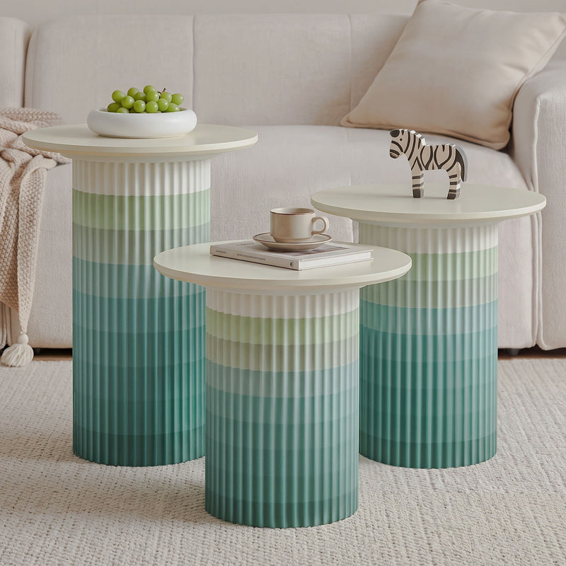 Set of three green ombré fluted side tables with cream round tops beside a sofa.