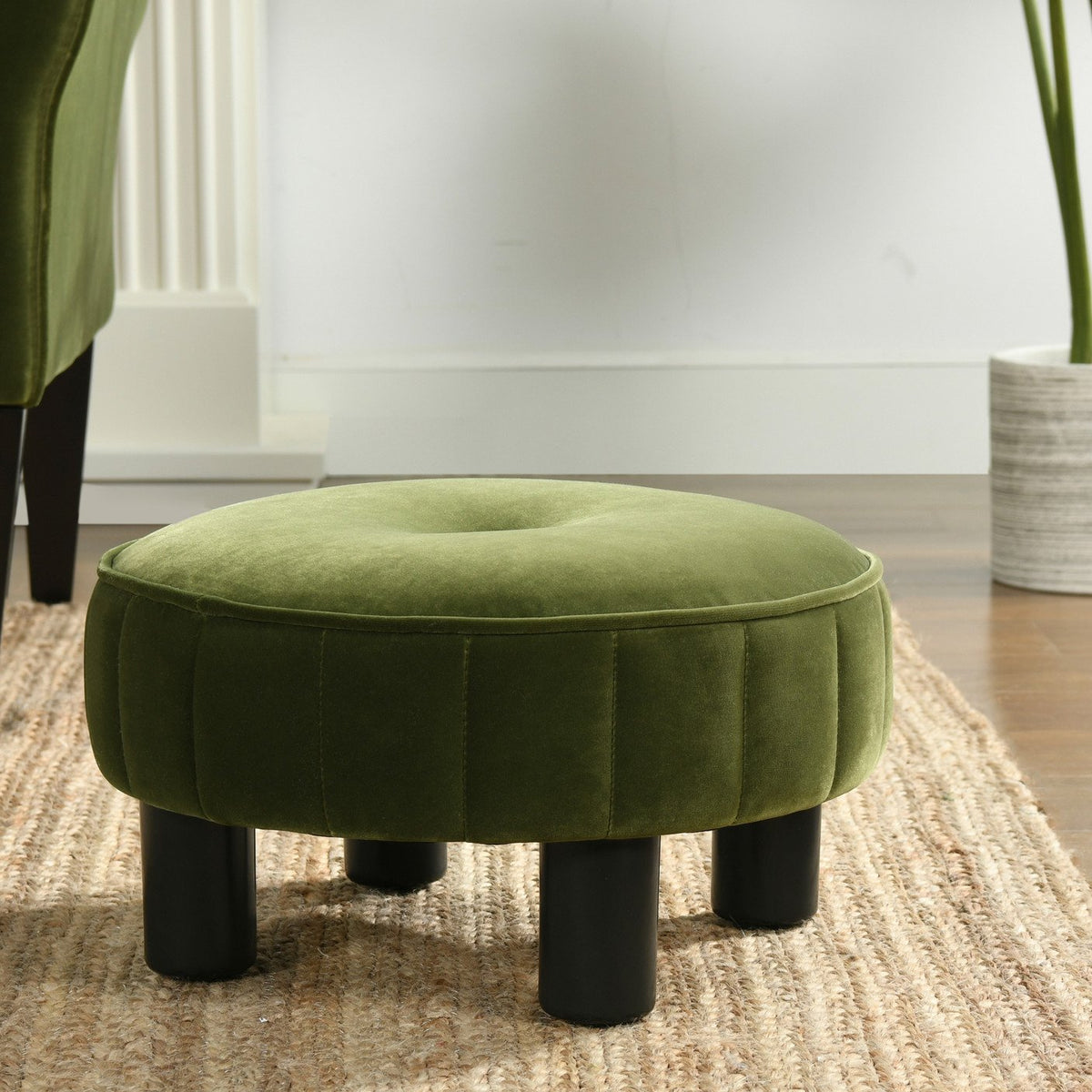 Olive green velvet round ottoman with short black legs in a room