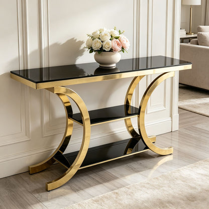 Black glass three-tier console with gold crescent supports styled beneath a vase in an entryway