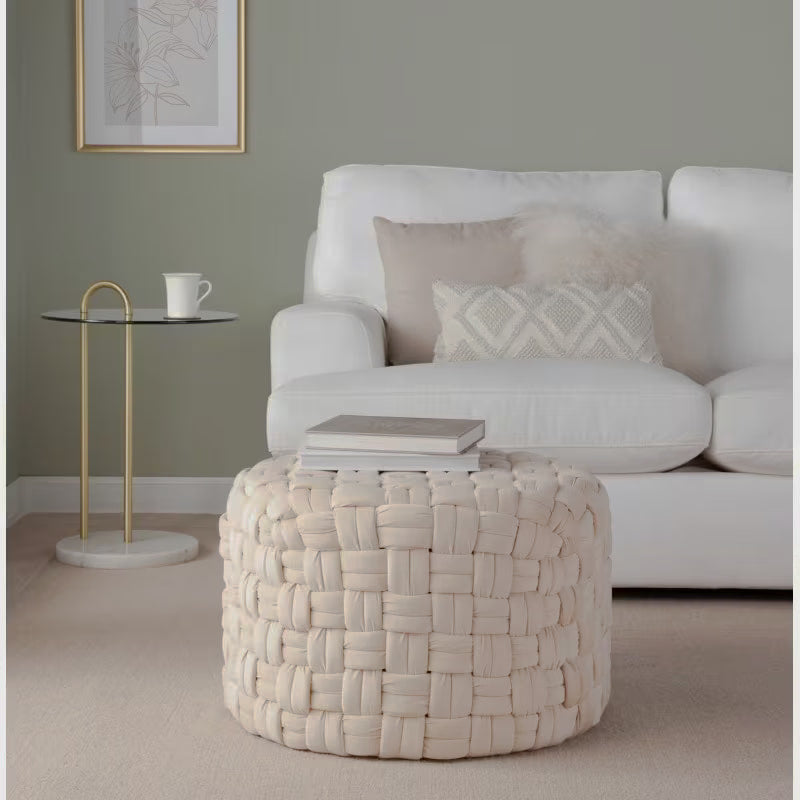 Cream basket-weave round ottoman styled with books in front of a white sofa