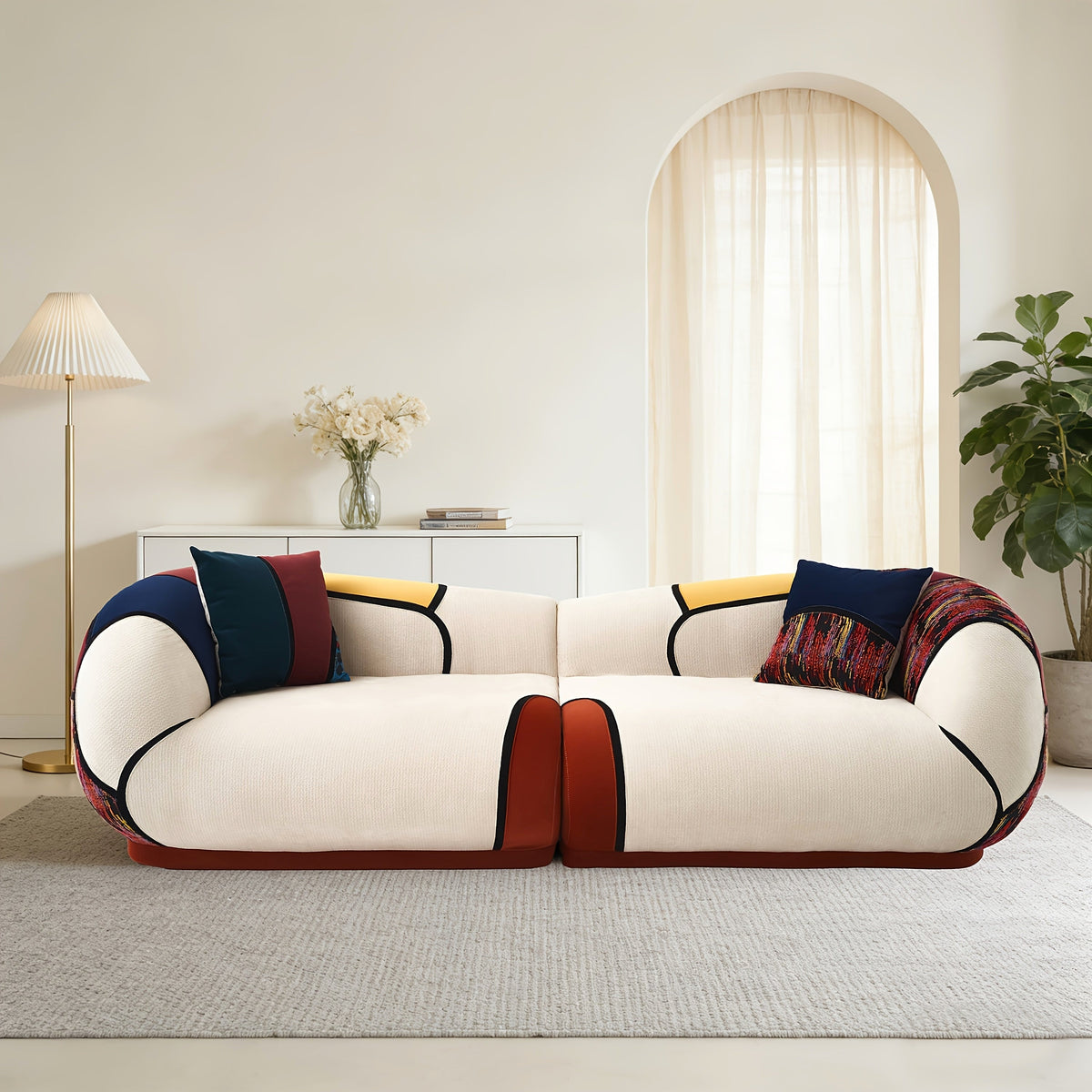 Front view of a cream curved sofa with dark piping, colorful panels and coordinating accent pillows.