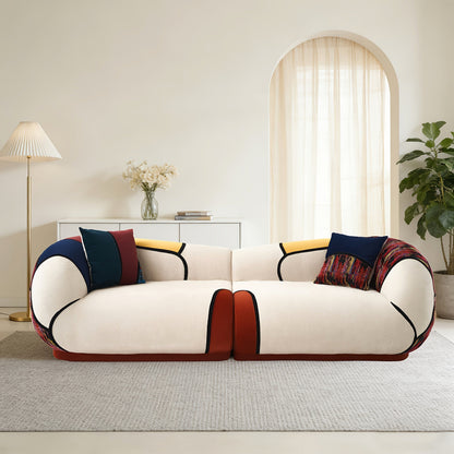 Front view of a cream curved sofa with dark piping, colorful panels and coordinating accent pillows.