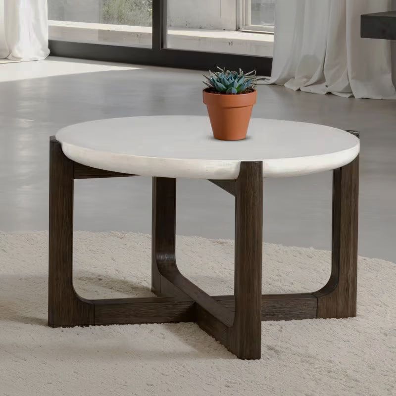 Round white stone-look coffee table with a dark crossed trestle base beside a window