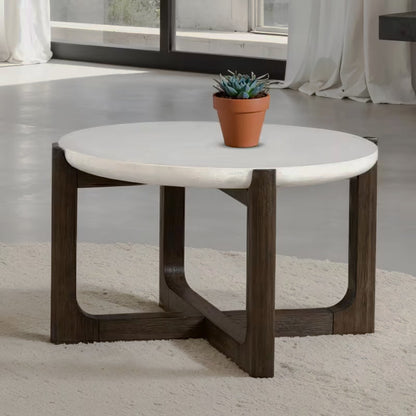 Round white stone-look coffee table with a dark crossed trestle base beside a window