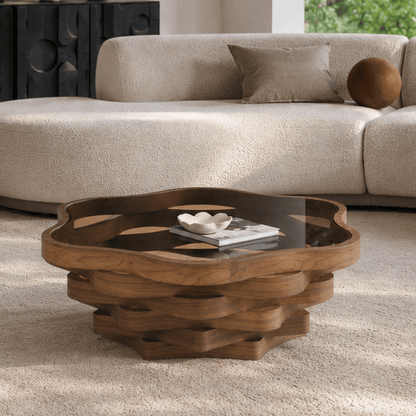 Cloud-shaped glass-top coffee table with a layered brown wave base beside a sofa