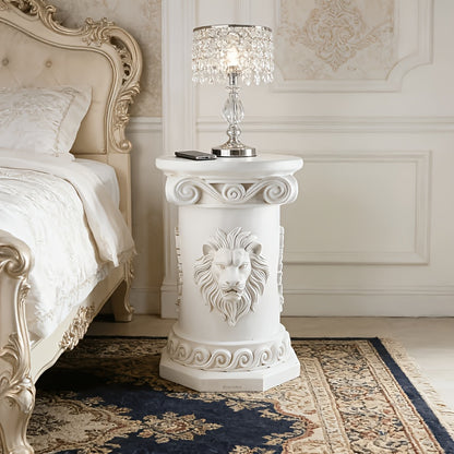 White pedestal table with a lamp beside a bed.