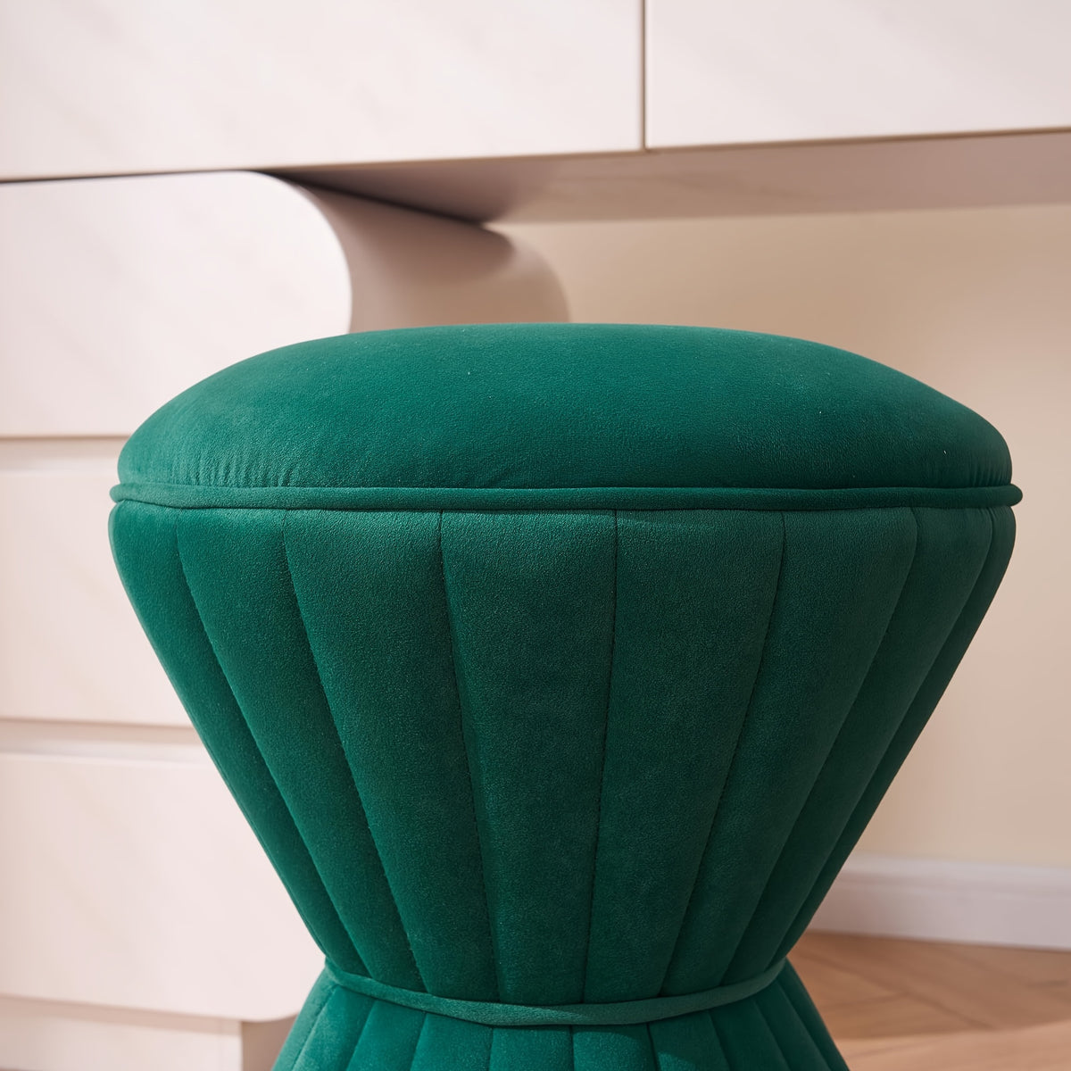 Close-up of the green ottoman's round padded top and piping