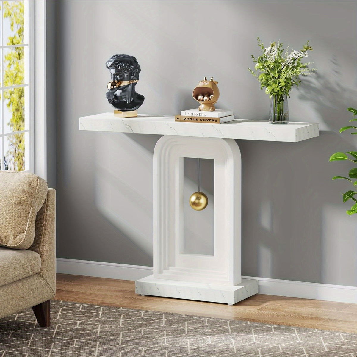 White arched pedestal console beside a living room chair with a vase and sculptural objects