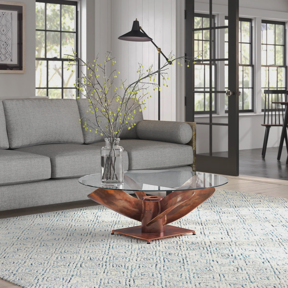 Round clear-top Archimedes coffee table with a sculptural copper-tone base beside a sofa