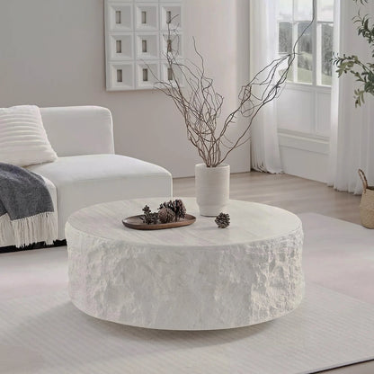Low round cream table with a pale stone-patterned top and rough textured sides in a bright room