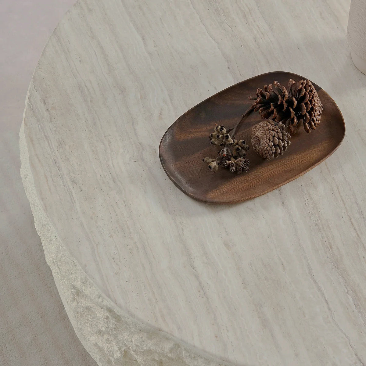 Overhead close-up of pale stone-patterned tabletop with a dark tray of pine cones