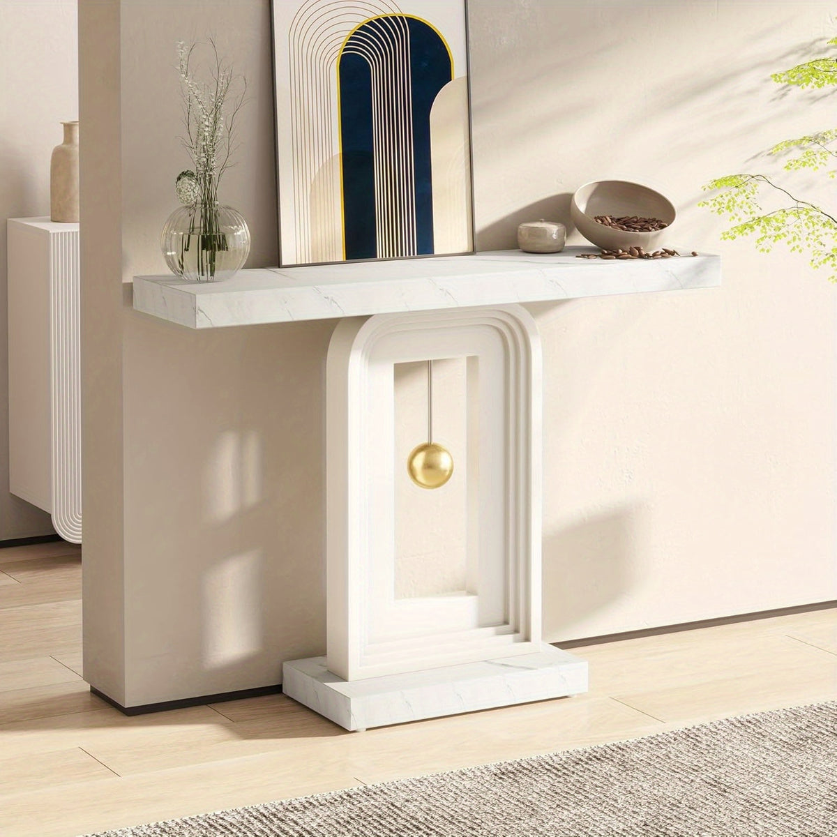 White console with gold sphere displayed against a pale wall in a sunlit hallway