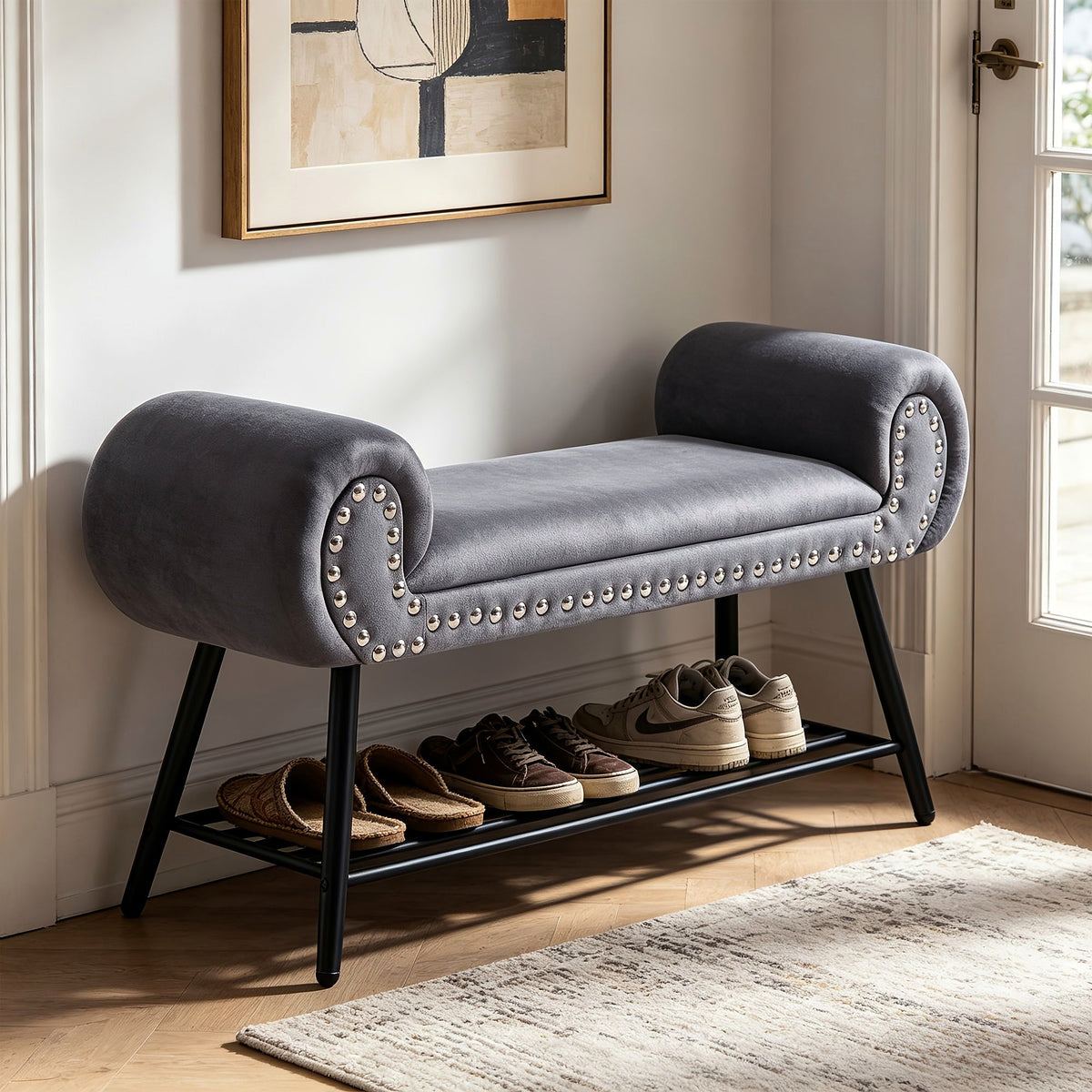 Gray rolled arm upholstered shoe bench with a black metal rack and silver tone nailheads