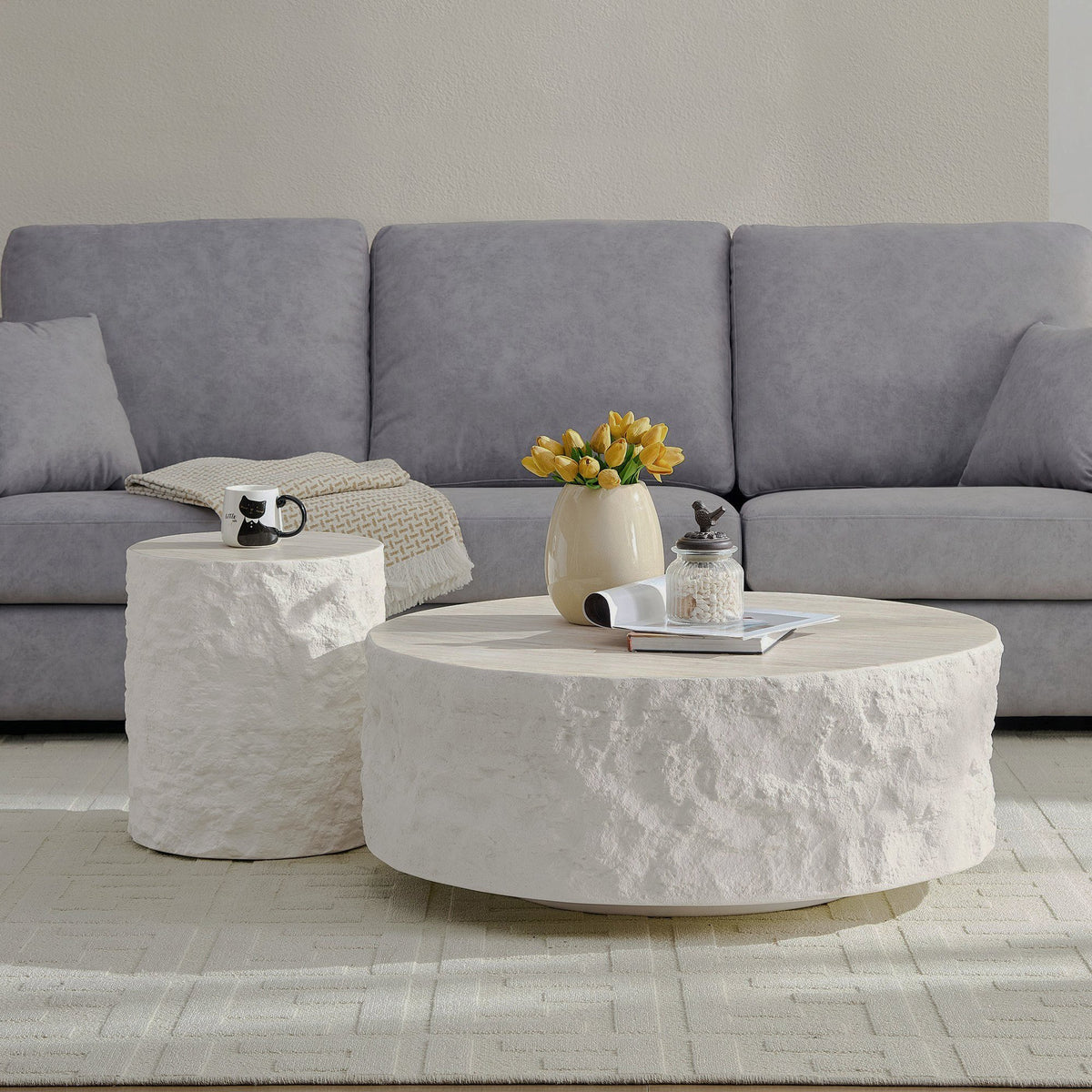Two cream round tables with textured stone-look sides in front of a gray sofa