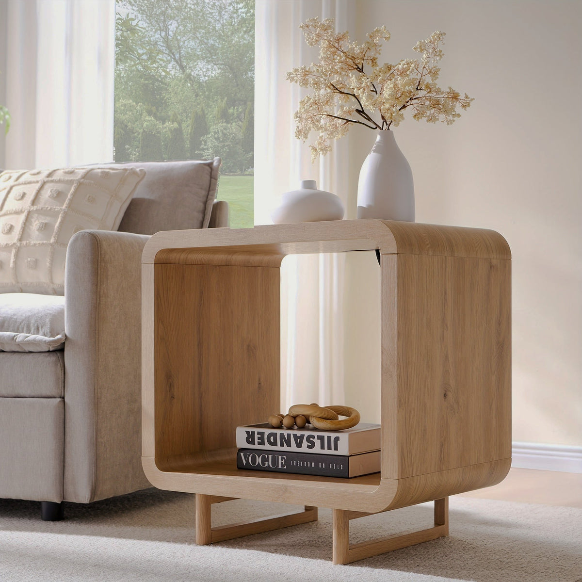 Natural wood-look end table with rounded corners, an open cubby and sled legs beside a gray sofa