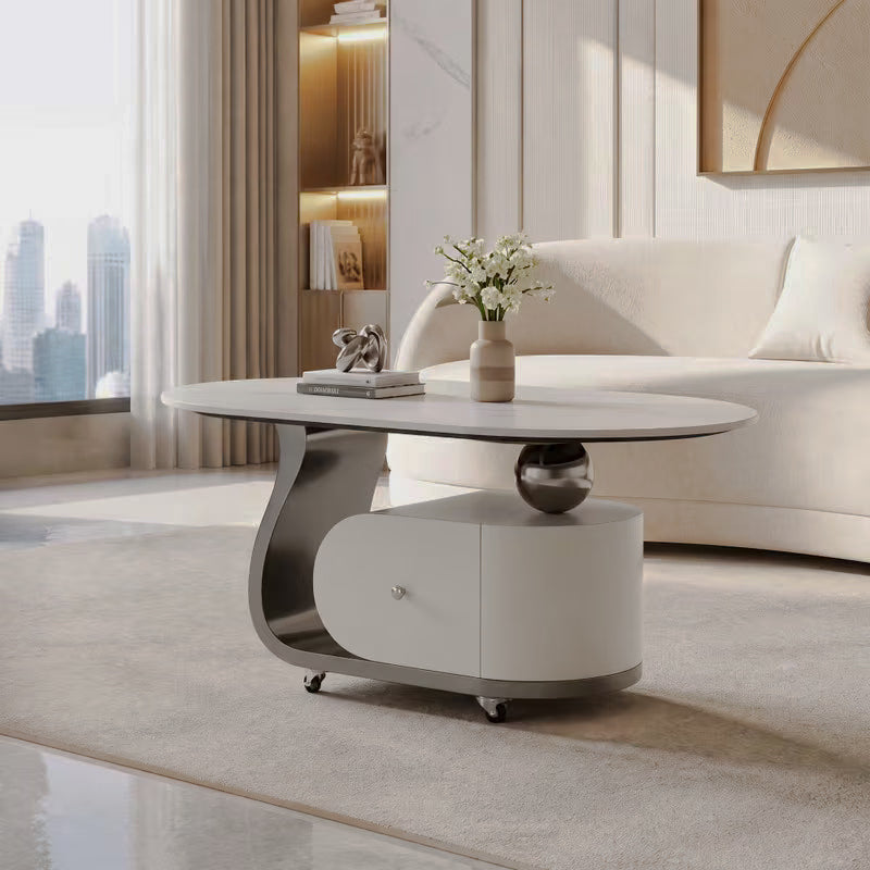 Cream coffee table with oval top, silver-tone curved frame and wheeled drawer base in a bright living room