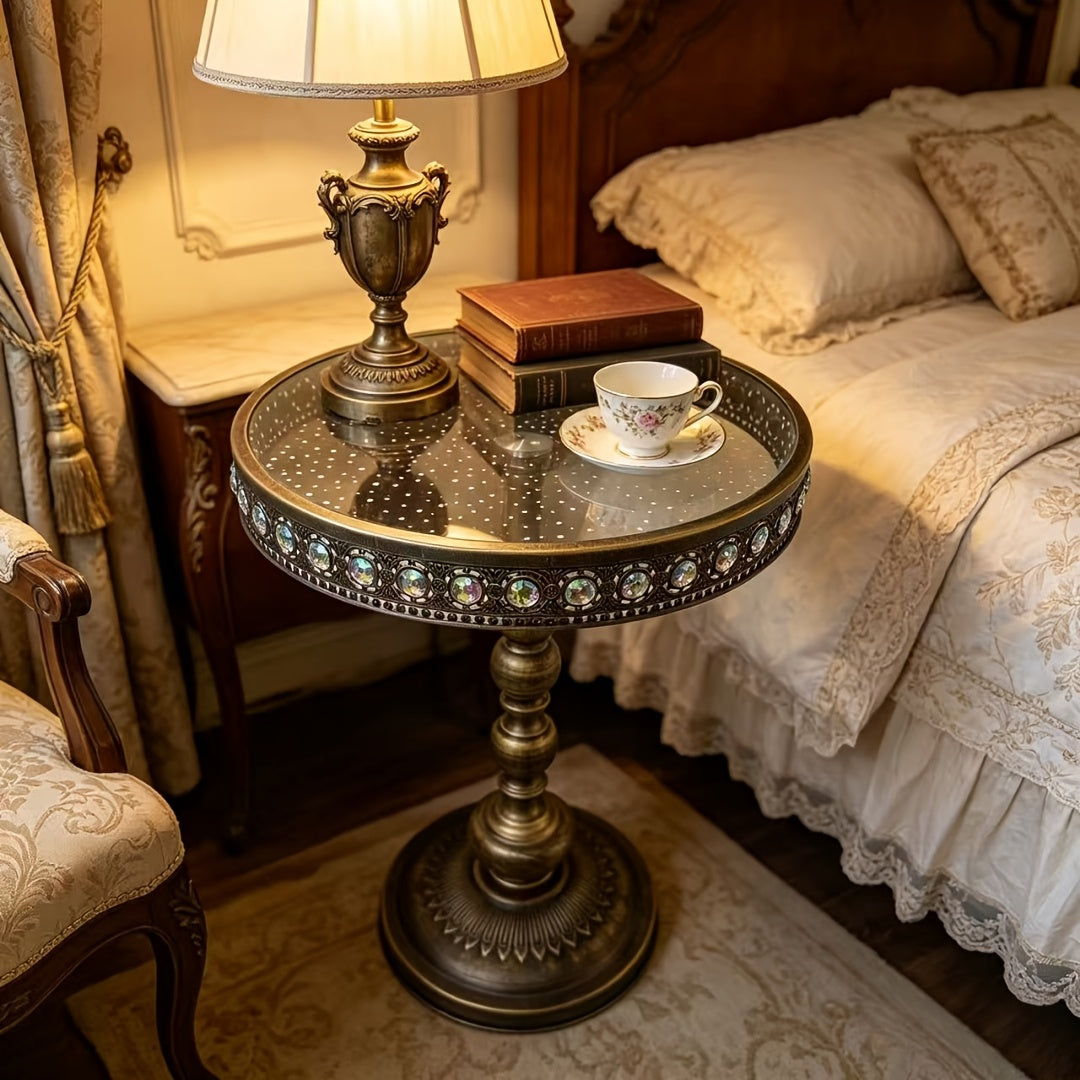 Bronze glass-top table used beside a bed and table lamp.