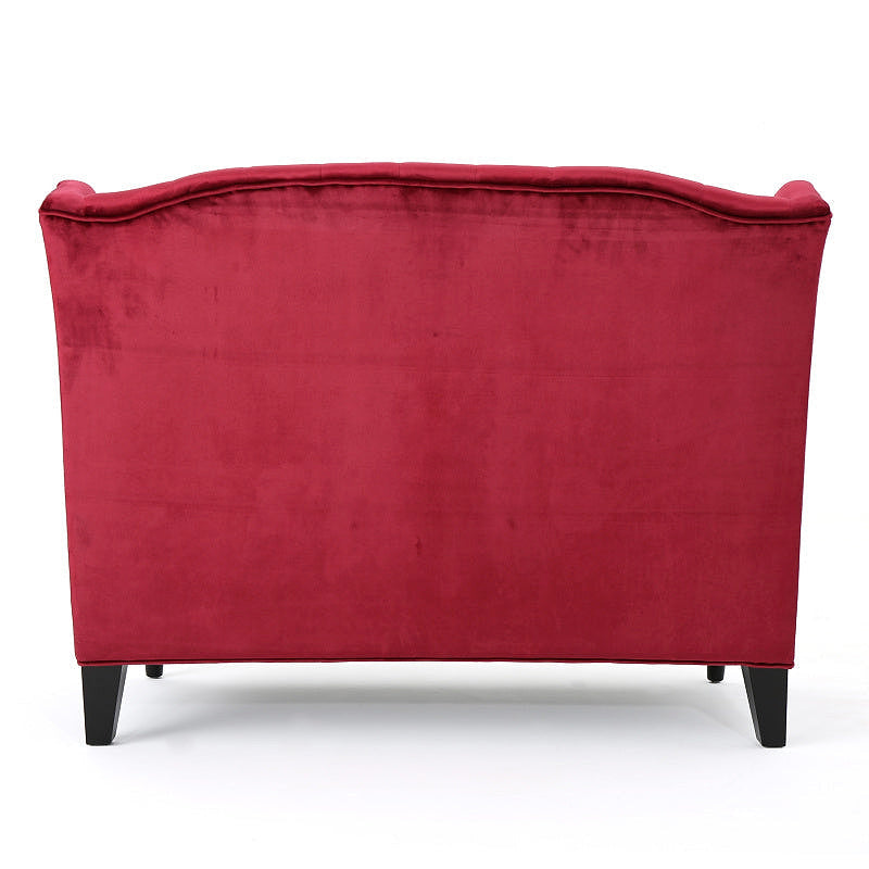 Rear view of the wine red velvet loveseat with a fully upholstered back and dark tapered rear legs.