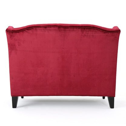Rear view of the wine red velvet loveseat with a fully upholstered back and dark tapered rear legs.