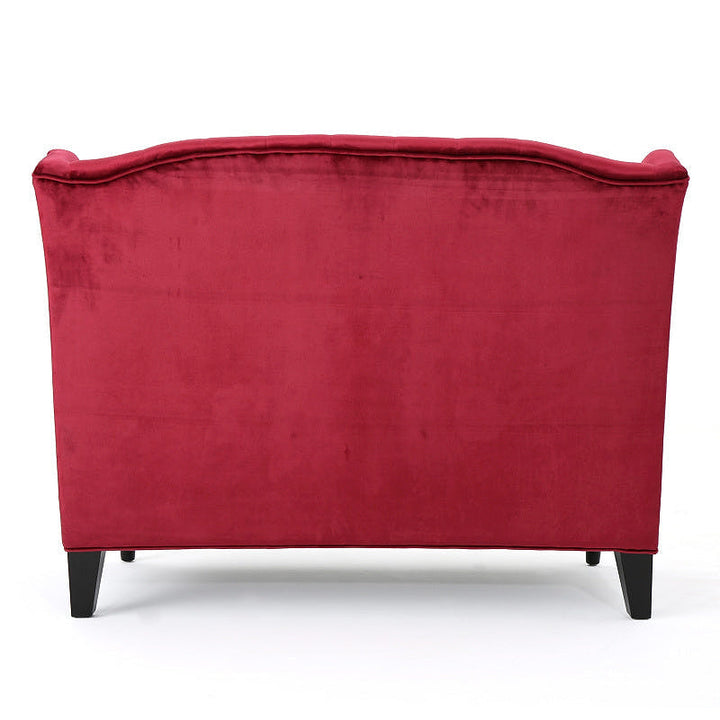 Rear view of the wine red velvet loveseat with a fully upholstered back and dark tapered rear legs.