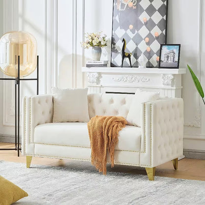 Beige tufted Chesterfield loveseat with two pillows and a draped throw