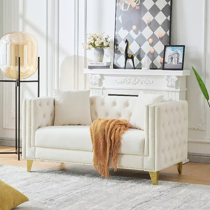 Beige tufted Chesterfield loveseat with two pillows and a draped throw
