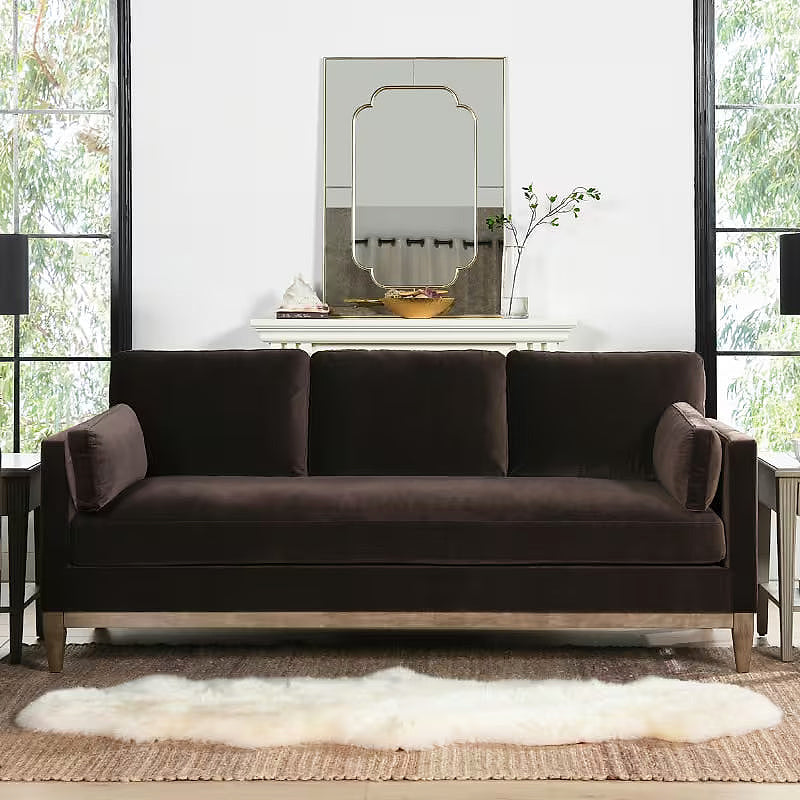 Knox deep brown velvet sofa with natural wood base in a living room