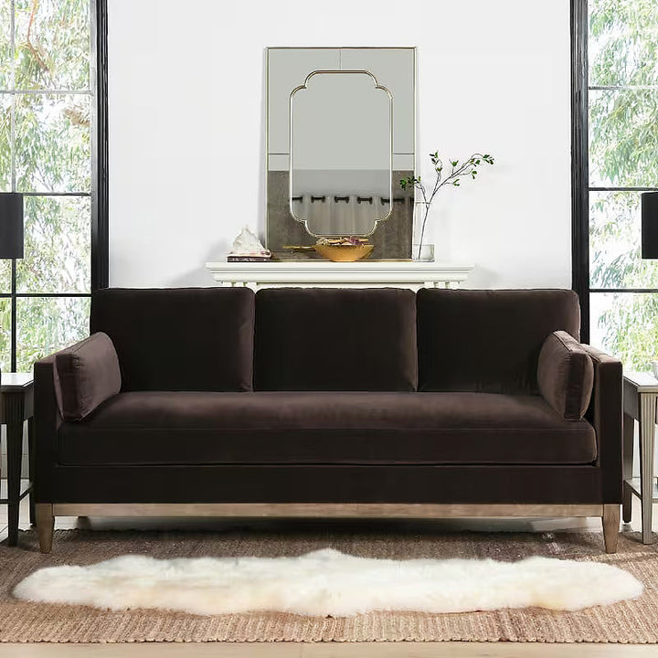 Knox deep brown velvet sofa with natural wood base in a living room