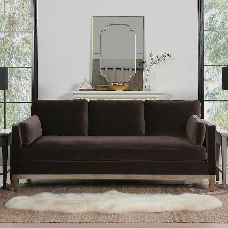 Knox deep brown velvet sofa with natural wood base in a living room