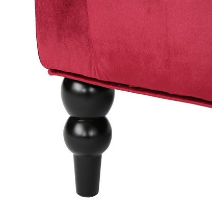 Close-up of a dark turned front leg beneath the wine red velvet loveseat.