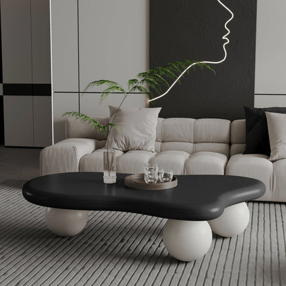 Black cloud-shaped coffee table with three white ball legs in front of a cream sofa