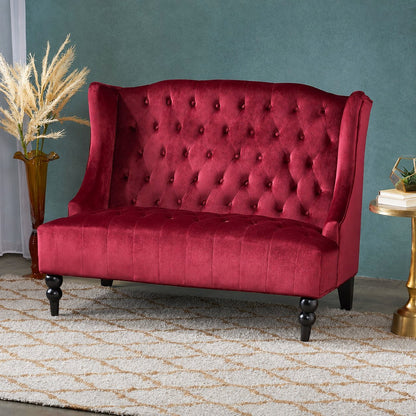 Wine red velvet loveseat with a button-tufted wingback and dark turned legs in a teal-walled room.