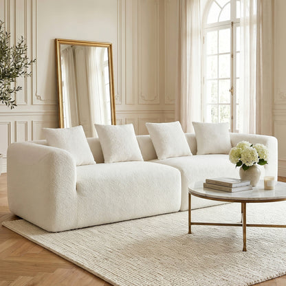 Angled view of the light neutral modular sofa, showing rounded arms and four coordinating pillows.